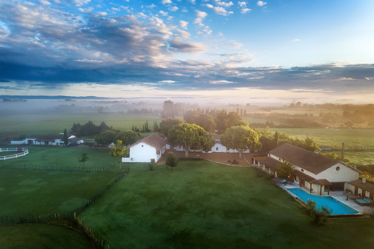 Vue aérienne du domaine au crépuscule, entre prairies et bâtiments provençaux.