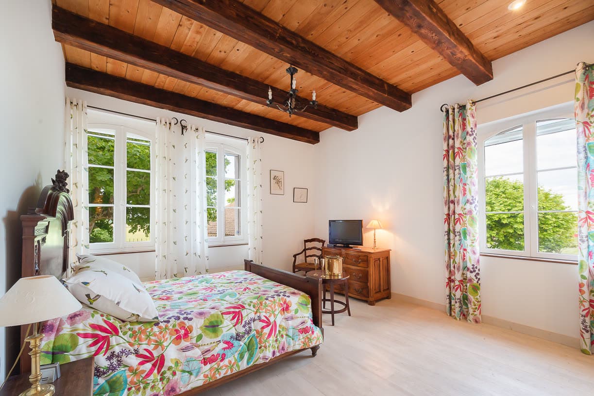 Une chambre en suite, poutres apparentes et tissus fleuris provençaux.
