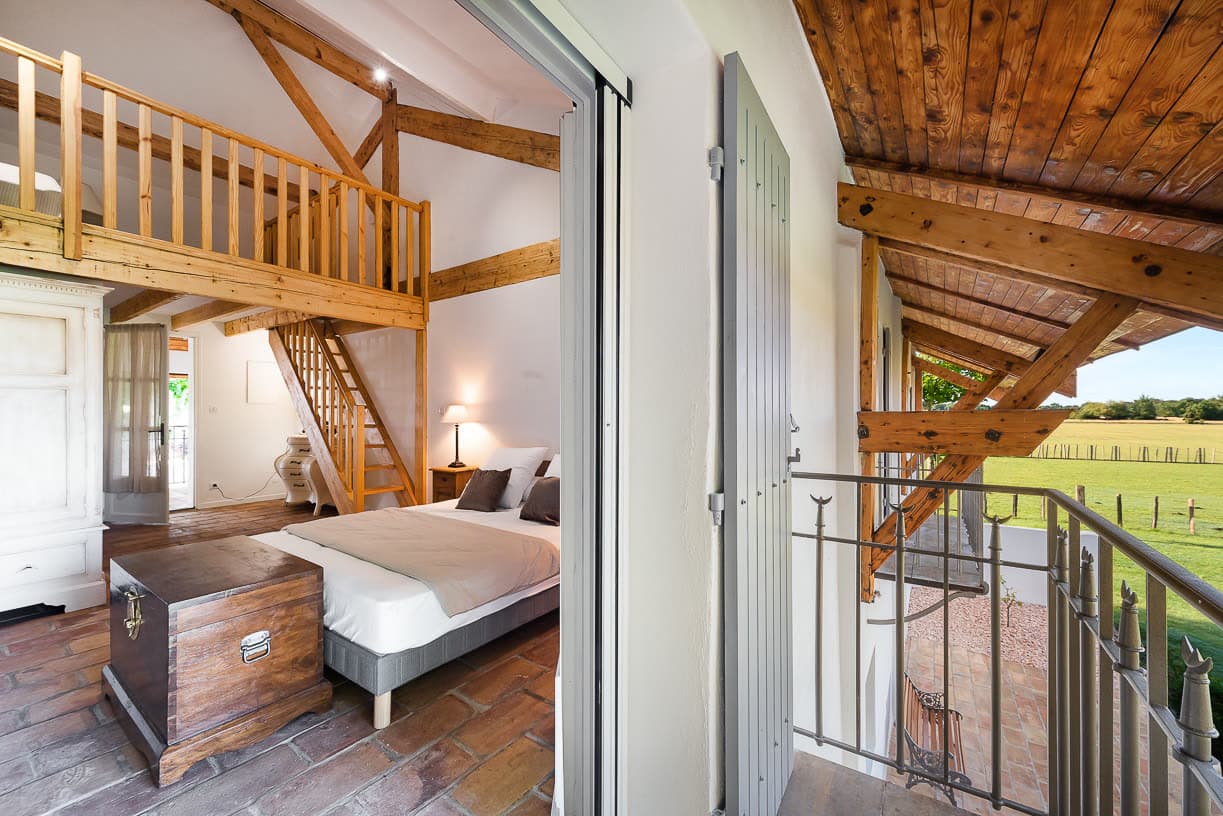 Une chambre en mezzanine, charpente ouverte et vue sur la campagne environnante.